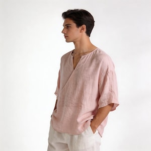 May include: A light pink linen top with a V-neck and short, wide sleeves. The top has a wrap-style design and is paired with off-white pants. The fabric appears lightweight and breathable, suitable for warm weather.