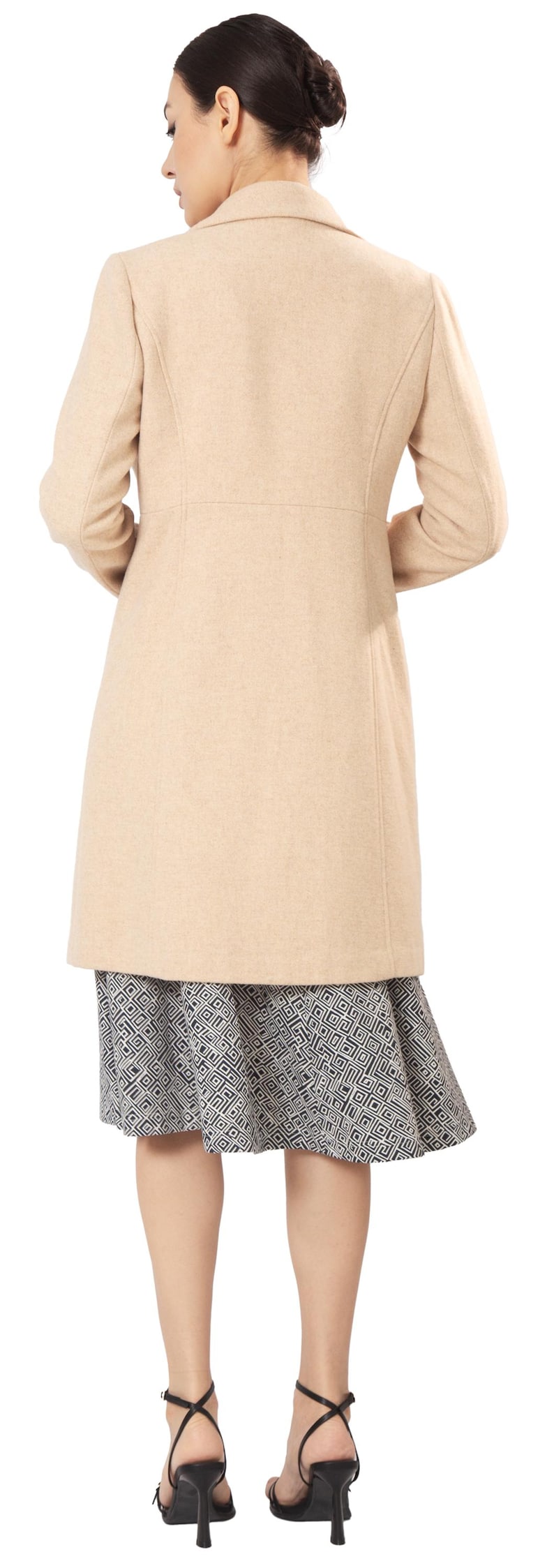Op de afbeelding: Een beige, knielange jas met een getailleerde pasvorm. De jas wordt gecombineerd met een rok met zwart-witte patronen. Het model draagt zwarte sandalen met hoge hakken. De afbeelding is van achteren genomen.