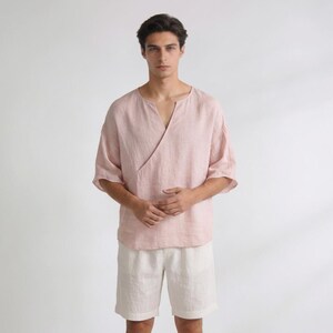 May include: A light pink linen wrap top with elbow-length sleeves and a V-neck. Paired with off-white linen shorts. The top has a wrap design that crosses over the chest. The outfit is made of a lightweight, breathable fabric.