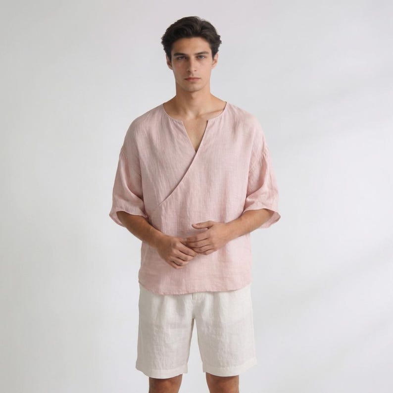 May include: A light pink linen wrap top with elbow-length sleeves and a V-neck. Paired with off-white linen shorts. The top has a wrap design that crosses over the chest. The outfit is made of a lightweight, breathable fabric.