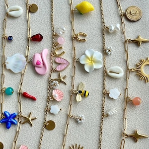 Peut inclure: Six chaînes à maillons dorés ornées de divers pendentifs, notamment une étoile de mer bleue, un chapeau de cow-boy rose, un citron jaune, une fleur blanche, une abeille, des coquillages, des soleils, des étoiles, des perles et des perles colorées.