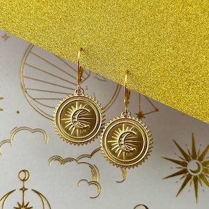 May include: Gold tone earrings with a sun and moon design. The earrings are circular and have a textured edge.