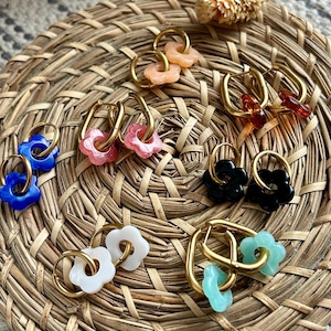 Peut inclure: Un ensemble de six paires de boucles d'oreilles créoles dorées avec des breloques de fleurs de différentes couleurs. Les breloques sont en plastique et sont disponibles en bleu, rose, blanc, noir, orange et vert.