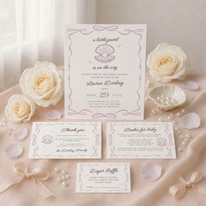 May include: A baby shower invitation suite with a pearl and seashell theme. The invitation and accompanying cards are light purple with elegant script and a pearl graphic. White roses and scattered pearls add to the delicate aesthetic.