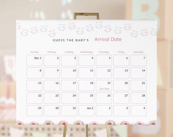 May include: A white baby shower calendar on a gold easel. The calendar is decorated with diaper and donut illustrations. The text reads "GUESS THE BABY'S Arrival Date" with a calendar grid for the month of December and January.