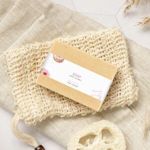 Może przedstawiać: Mydło w kostce z białą etykietą, na której widnieje napis "SOAP SWEET & BUBBLY BETTY'S BABY SHOWER". Mydło znajduje się w białym siateczkowym woreczku, a na etykiecie są narysowane pączki.