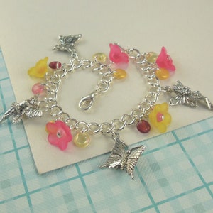 Girls pewter charm bracelet with 4 total charms, 2 different fairies and 2 different butterflies interspersed with acrylic flowers and glass drops in various shades of pink and yellow.