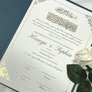 May include: A white card with gold calligraphy and text. The text reads "This agreement is to certify the marriage of Hamza & Sophia" and includes the date "2nd January 2024" and the location "In the city of Leicester, United Kingdom".