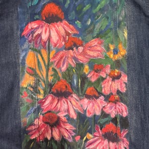 May include: Denim jacket with a hand-painted floral design. The artwork features pink coneflowers with orange centers against a blue and green background. The jacket is made of blue denim.