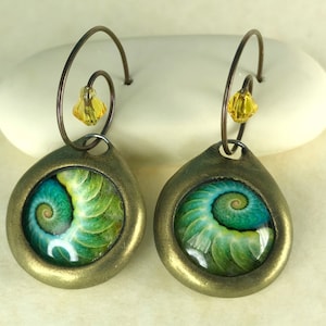 May include: A pair of bronze-colored earrings with a green and blue spiral design. Each earring features a small yellow crystal at the top.