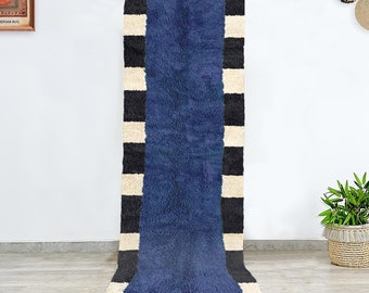 May include: A long, narrow blue rug with black and white stripes. The rug is hanging on a white wall.