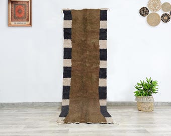 May include: A long, brown rug with black and white stripes running down the sides. The rug is hanging on a white wall.