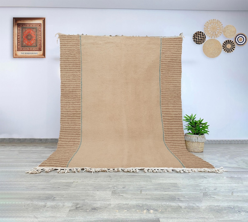 Hand knotted Moroccan Beni Ourain rug in neutral beige with minimalist design, featuring soft striped textured borders, woven in wool by Berber artisans, perfect for Japandi, Scandinavian, or modern interiors.