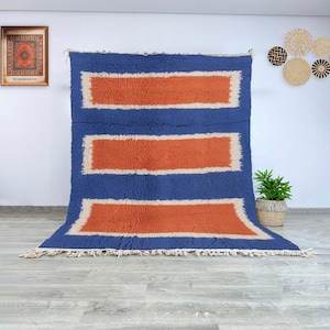 Authentic Beni Ourain Moroccan wool rug featuring a modern composition of terracotta rectangular panels framed by cream and deep blue borders. Handwoven by Berber women in the Atlas Mountains using natural wool, this rug combines traditional Moroccan weaving techniques with a bold geometric aesthetic. Its soft, plush texture and contrasting colors make it a stunning centerpiece for modern, bohemian, or Scandinavian interiors seeking warmth, structure, and authentic handmade artistry.