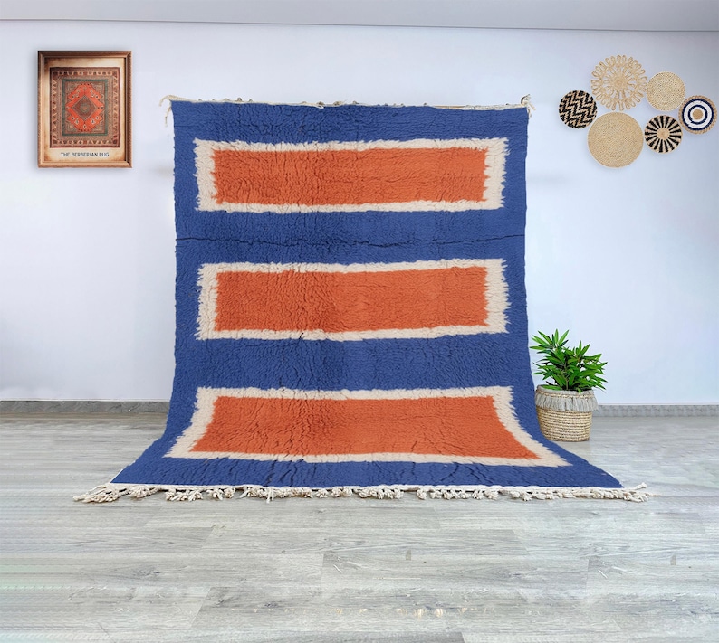 Authentic Beni Ourain Moroccan wool rug featuring a modern composition of terracotta rectangular panels framed by cream and deep blue borders. Handwoven by Berber women in the Atlas Mountains using natural wool, this rug combines traditional Moroccan weaving techniques with a bold geometric aesthetic. Its soft, plush texture and contrasting colors make it a stunning centerpiece for modern, bohemian, or Scandinavian interiors seeking warmth, structure, and authentic handmade artistry.