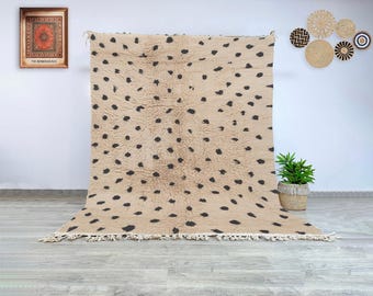 May include: Beige and black spotted area rug with a fringe. The rug has a soft, textured appearance and a pattern of dark spots scattered across the surface. The rug is displayed indoors.