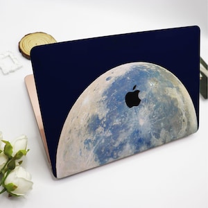 May include: A navy blue laptop skin with a full-color image of the moon. The moon has a detailed, realistic texture and a black Apple logo is visible on the skin.