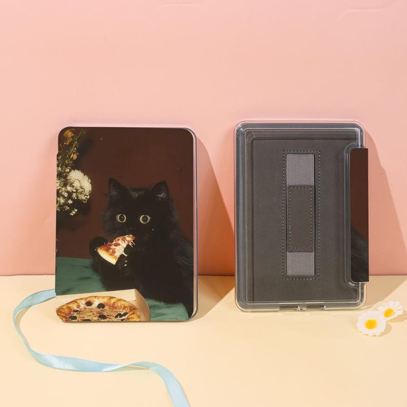 May include: A black cat eating pizza is featured on a rectangular case. The case is open, revealing a gray interior with a strap. A second case is closed, displaying the cat image. A blue ribbon and daisy-shaped decorations are also present.