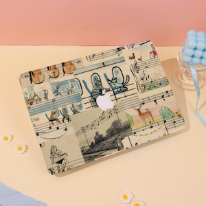 Può includere: Una custodia per laptop con un design stravagante con note musicali, gatti dei cartoni animati e altre illustrazioni. La custodia ha uno sfondo beige chiaro con accenti colorati, tra cui arancione, blu e verde. Il logo Apple è visibile.