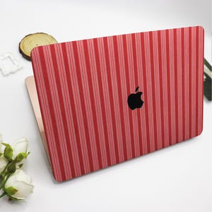 May include: A red laptop skin with a vertical white stripe pattern. The skin covers the back of a laptop, with the black Apple logo visible. The laptop is open, revealing a gold-colored interior.