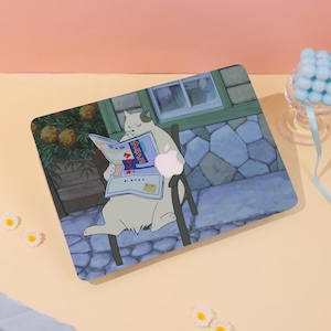 Könnte beinhalten: Eine Laptop-Hülle mit einer Illustration einer Katze, die eine Zeitung liest. Die Katze ist weiß mit grauen Flecken. Der Hintergrund zeigt ein Gebäude mit Steinmauern und einem Fenster. Die Hülle hat ein Apple-Logo.
