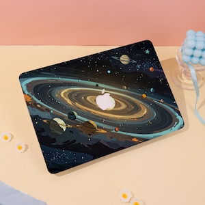 May include: A laptop case featuring a colorful illustration of a galaxy with planets, stars, and swirling nebulas. The design includes a white apple logo at the center. The case is black with a glossy finish, and the overall theme is space and astronomy.