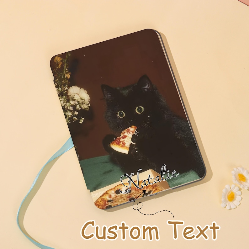 May include: A rectangular custom notebook featuring a black cat eating pizza. The notebook has a brown background with the text "Custom Text" and the name "Natalie" in cursive. A light blue ribbon is attached.