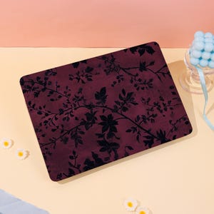 May include: A rectangular laptop skin featuring a dark burgundy background with a black silhouette pattern of sprawling leafy branches and small berries. The design covers the entire top surface of the device in a flat, matte-style finish.