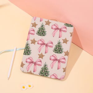 May include: A rectangular tablet case with a festive pattern. The design features pink bows, green Christmas trees, and gingerbread stars on a light beige background. A white stylus and a light blue ribbon are visible.
