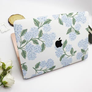May include: A white laptop computer with a floral design featuring blue hydrangeas and green leaves. The laptop has a black Apple logo.