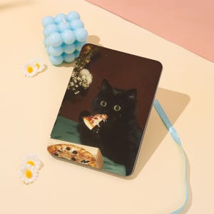 May include: A rectangular black cat-themed decorative tray featuring a black cat eating pizza. The tray has a dark brown background with a green tablecloth. A small pizza box is visible. A light blue bubble candle and daisy-shaped decorations are in the background.