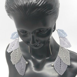 May include: A pair of long, silver dangle earrings with three layered feather-shaped charms in shades of light blue and gray.