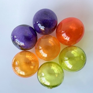 May include: Seven glass balls in various colors, including purple, orange, and green. The balls are arranged in a circle on a white background.