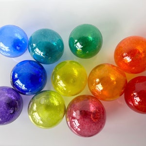 May include: A collection of eleven colorful glass marbles in shades of blue, green, yellow, orange, and red. The marbles are round and have a glossy, reflective surface, creating a vibrant display of color.