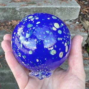 May include: A blue glass orb with white and green speckles. The orb has a clear glass base.