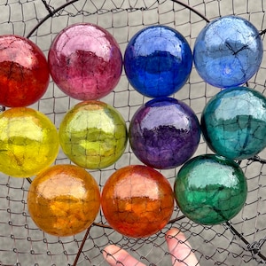 May include: Ten glass ornaments in a wire basket. The ornaments are all different colors, including red, blue, green, yellow, and purple. Each ornament has a textured surface.