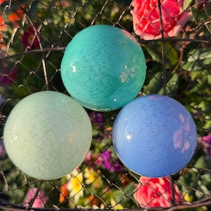 May include: Three smooth, spherical glass orbs featuring a crackled texture. The top orb is a vibrant turquoise, the bottom left orb is a pale mint green, and the bottom right orb is a soft periwinkle blue, all displaying a glossy finish.