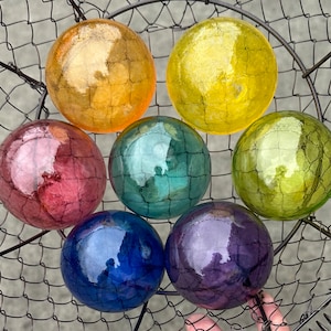 May include: Seven glass orbs in a wire basket. The orbs are iridescent and have a textured surface. The colors are yellow, green, blue, purple, and pink.