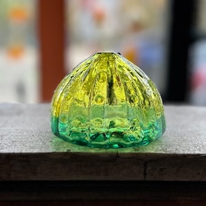 May include: A decorative glass object with a rounded, ridged shape. The glass transitions from a vibrant yellow at the top to a deep green at the base. The surface has a textured, bubbly appearance, creating a unique visual effect.