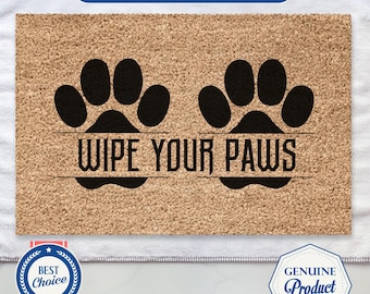 May include: A rectangular doormat made of natural coir fiber. The mat features two large black paw prints and the text "WIPE YOUR PAWS" in a bold, black font. The mat is designed to be placed at an entryway.