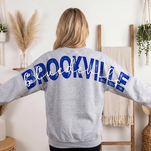 Może przedstawiać: Szara bluza z napisem "BROOKVILLE" w dużych, niebieskich literach na plecach. Słowo "blue devils" jest napisane kursywą nad słowem "BROOKVILLE".