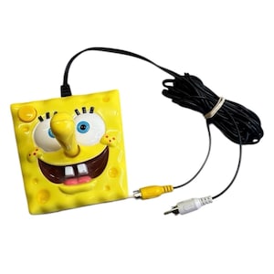 May include: A yellow, square-shaped video game controller featuring the face of the cartoon character SpongeBob SquarePants. The controller has a long black cable with yellow and white connectors.