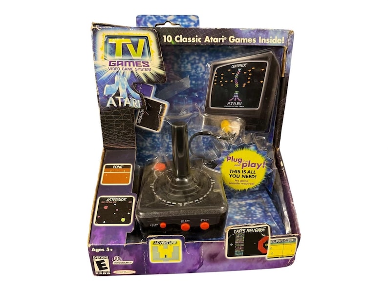 以下が含まれることがあります： 箱入りのAtari TV Gamesビデオゲームシステム。パッケージには、Atariのロゴ、ゲームタイトル、ジョイスティックコントローラーが描かれています。箱には「10 Classic Atari Games Inside!」と「Plug and play!」の文字が含まれています。