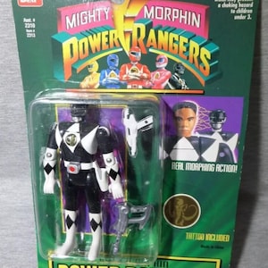 May include: A packaged Mighty Morphin Power Rangers action figure. The figure is black and white with accessories. The packaging is green and yellow with the Power Rangers logo and images of the characters. The package includes the text "Real Morphing Action!" and "Tattoo Included".