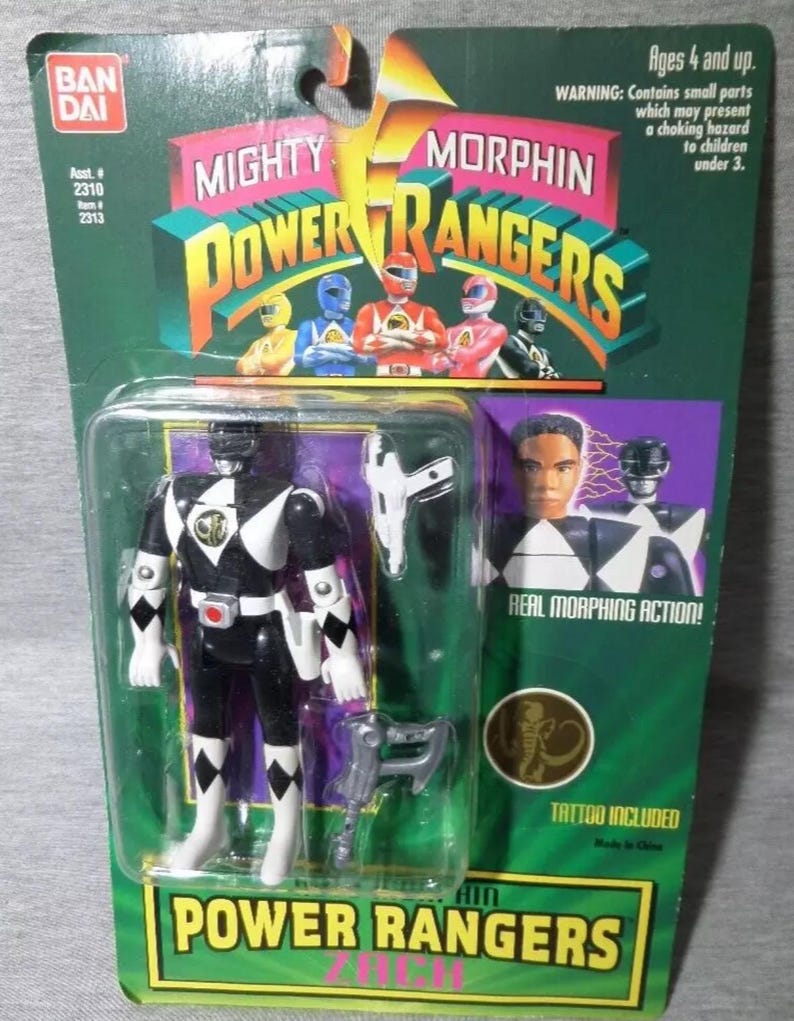 May include: A packaged Mighty Morphin Power Rangers action figure. The figure is black and white with accessories. The packaging is green and yellow with the Power Rangers logo and images of the characters. The package includes the text "Real Morphing Action!" and "Tattoo Included".
