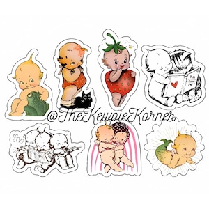 May include: Set of seven vintage-style stickers featuring cute cartoon babies in various poses. The stickers are printed on white paper with a glossy finish. The stickers feature a baby dressed as a strawberry, a baby reading a book, a baby holding a frog, a baby holding a cat, two babies playing music, two babies hugging, and a baby with a mermaid tail.