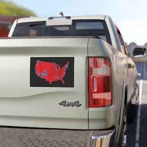 May include: A black and red sticker of the United States map with blue county outlines on the back of a grey pickup truck.