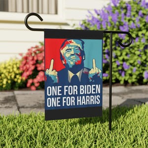 May include: A black garden flag with a graphic of a man giving the middle finger. The background is red and blue. The text "ONE FOR BIDEN ONE FOR HARRIS" is printed in white.