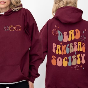 May include: A maroon hoodie with a front pocket and a drawstring hood. The front features three smiley face designs. The back of the hoodie displays the text "DEAD PANCREAS SOCIETY" in a retro font, with smiley faces and stars.