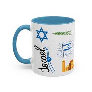 Pode incluir: Caneca de cerâmica branca com interior e alça azuis. A caneca é decorada com símbolos israelenses, incluindo uma Estrela de David, uma bandeira e a palavra "Israel" em escrita. O design também apresenta uma ilustração de um edifício.